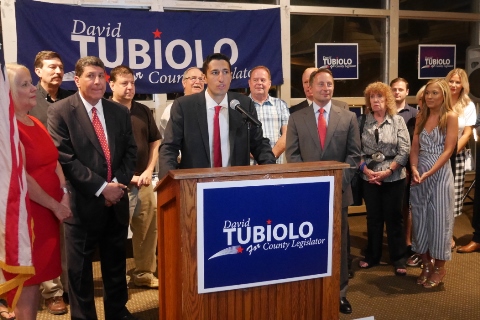 David Tubiolo speaks at podium surrounded by supporters