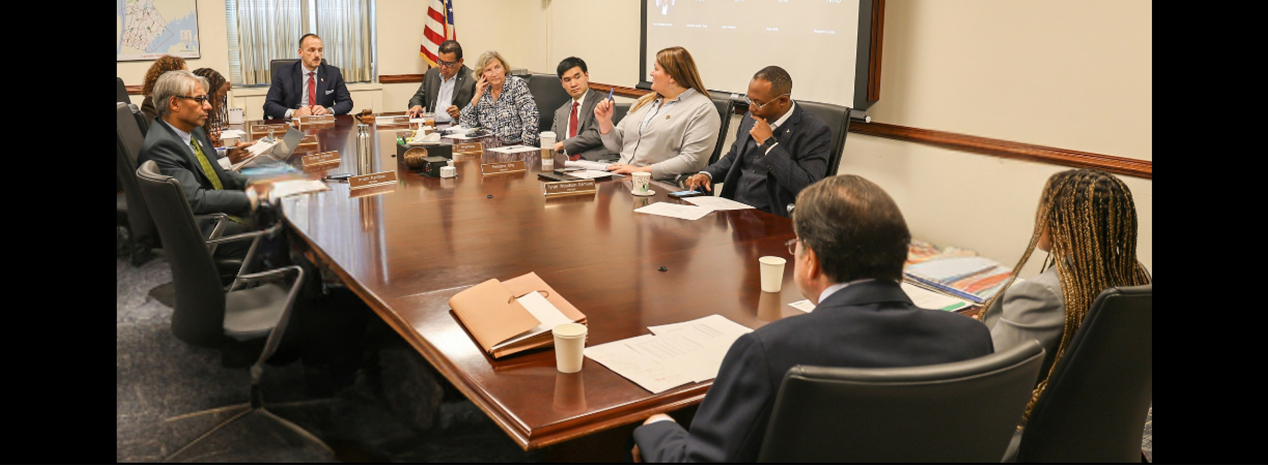 Legislators and guests seated around a conference table during a committee meeting.