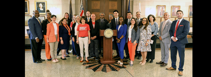Legislators, community leaders, and advocates gathered around a podium during a press conference in a board rotunda.